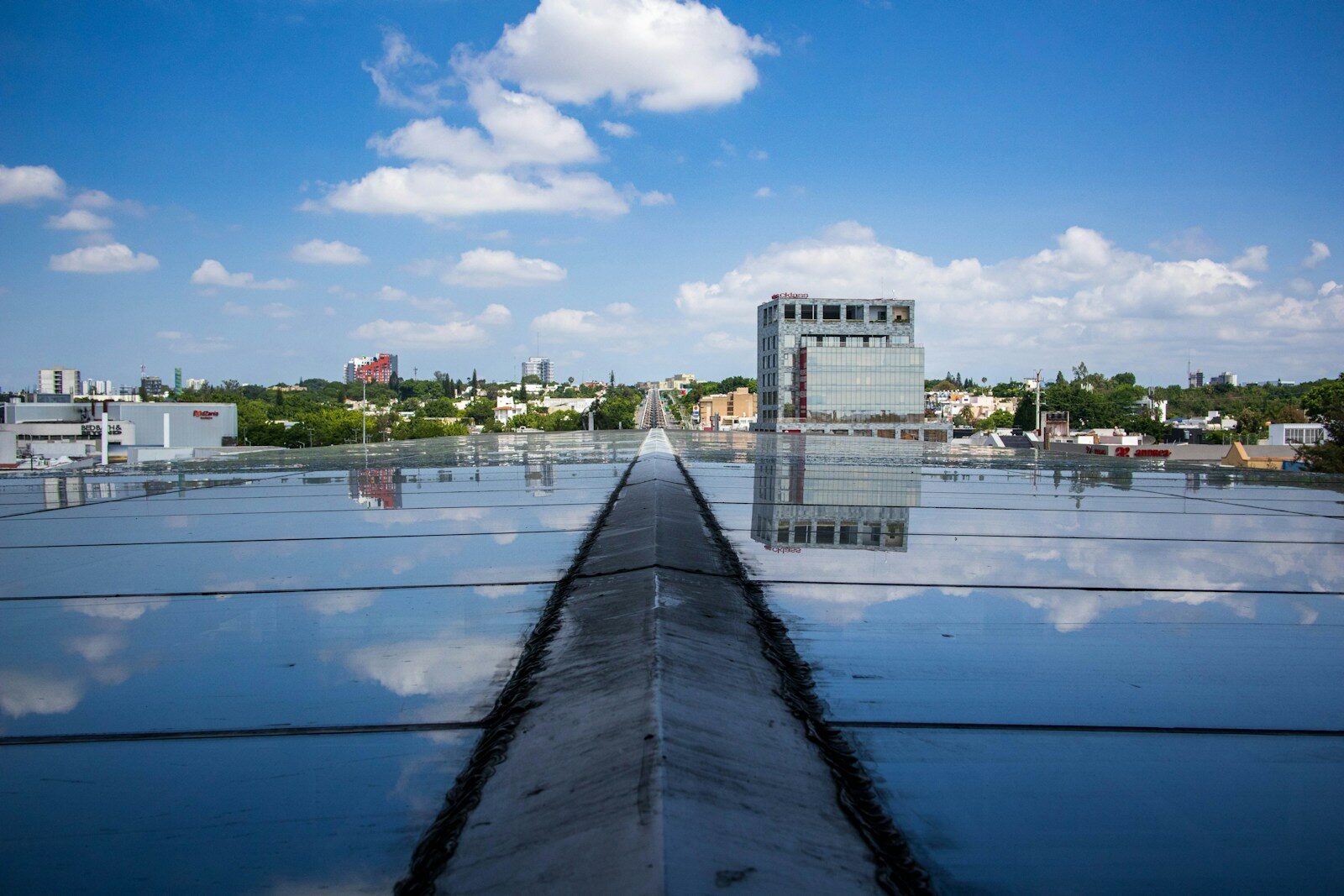 Reflective rooftop surface with a distant building under blue sky